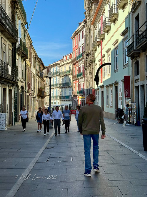 A person walking down a narrow street lined with colorful buildings and shops in a picturesque European city.