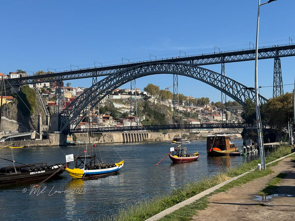 View of a bridge spanning a river, with traditional boats moored in the water and colorful buildings on the hillside.