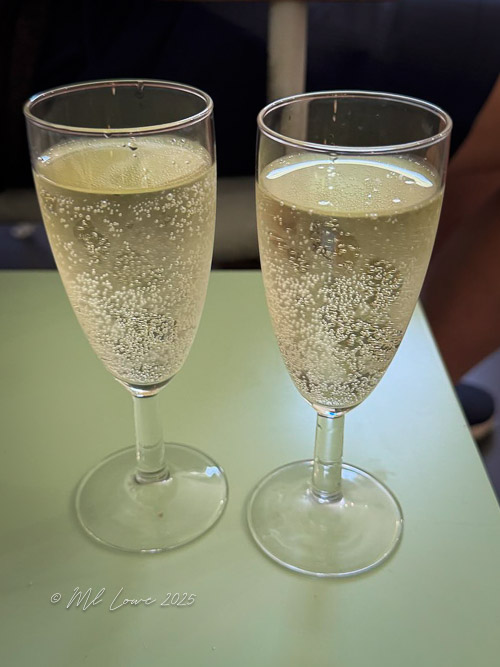 Two glasses of sparkling wine filled with bubbles on a light green table.