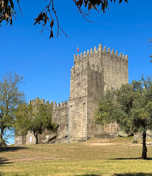 A medieval fortress with tall stone walls and battlements under a clear blue sky.