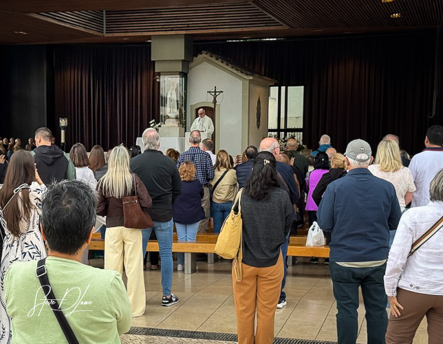 A large group of people gathered in a religious setting, listening attentively to a speaker at the front.