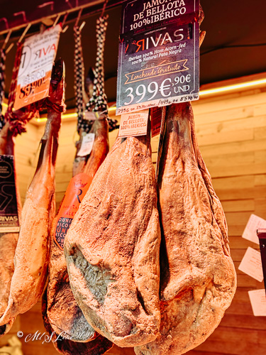 Hanging cured Ibérico ham with a price tag in a market setting.