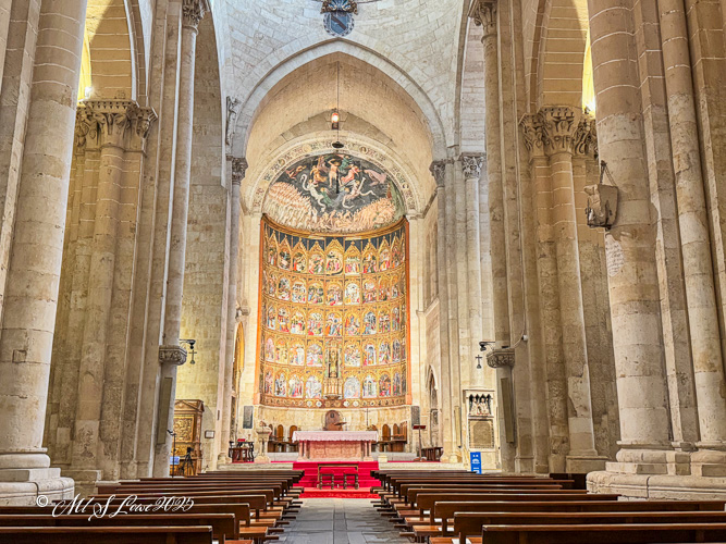 Interior view of a historic church featuring ornate decorations, high stone columns, and a colorful altar with intricate artwork and a tapestry.