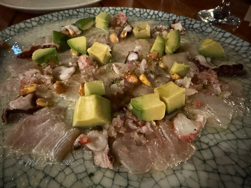 A plate of ceviche featuring assorted seafood, chopped avocado, and garnished with crunchy ingredients.