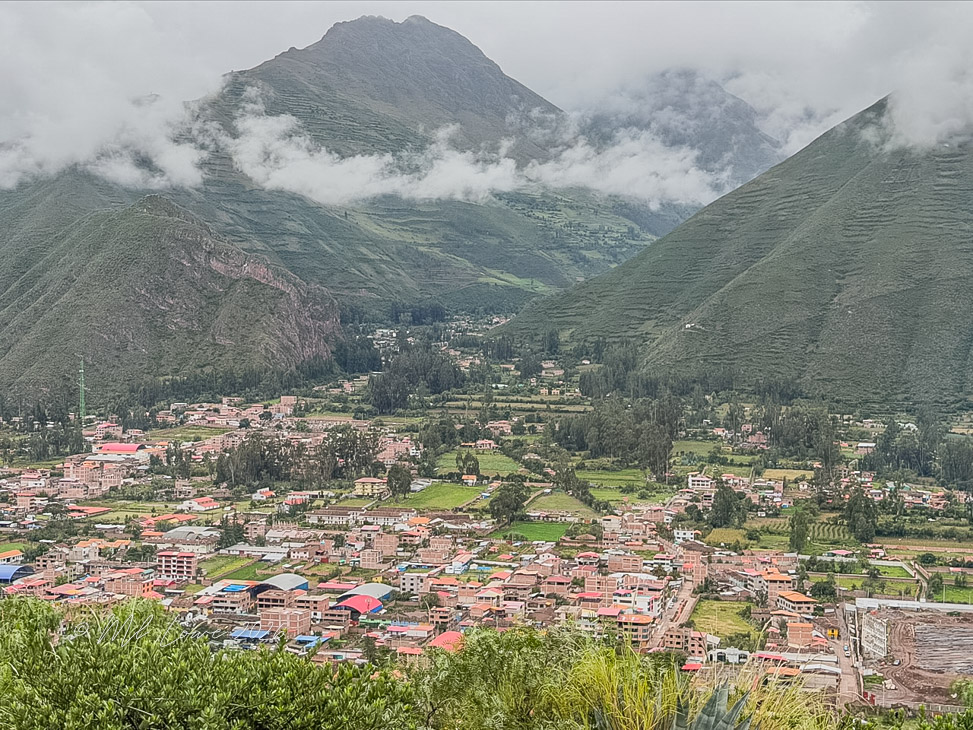 A panoramic view of a town nestled in a valley surrounded by lush green mountains and partly cloudy skies.