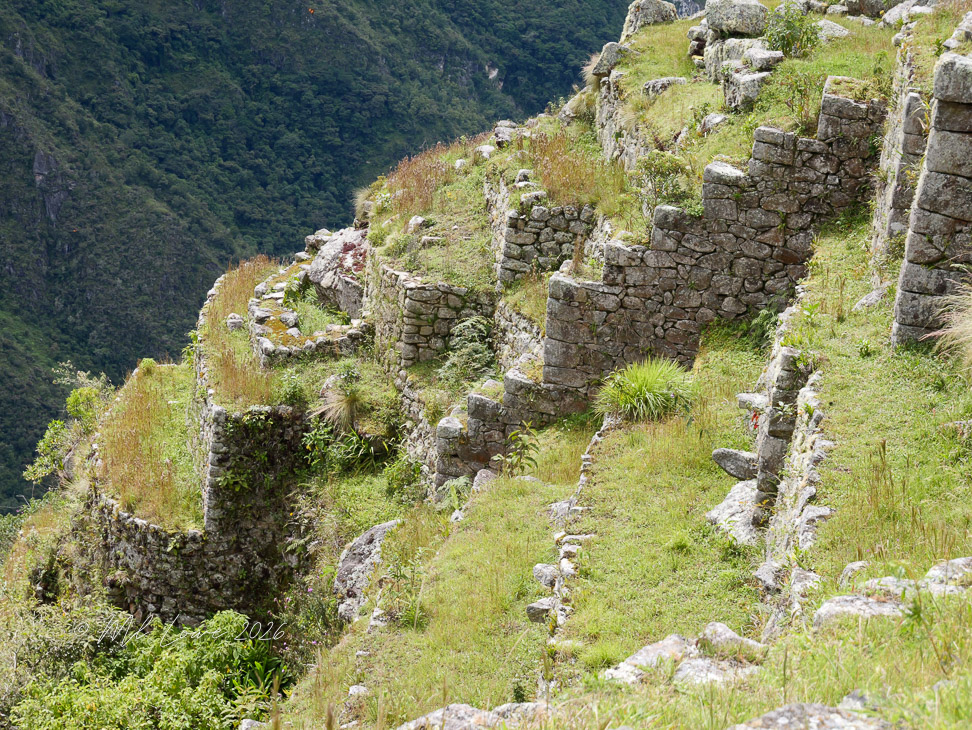 Ancient stone ruins on a grassy hillside overlooking a mountainous landscape.