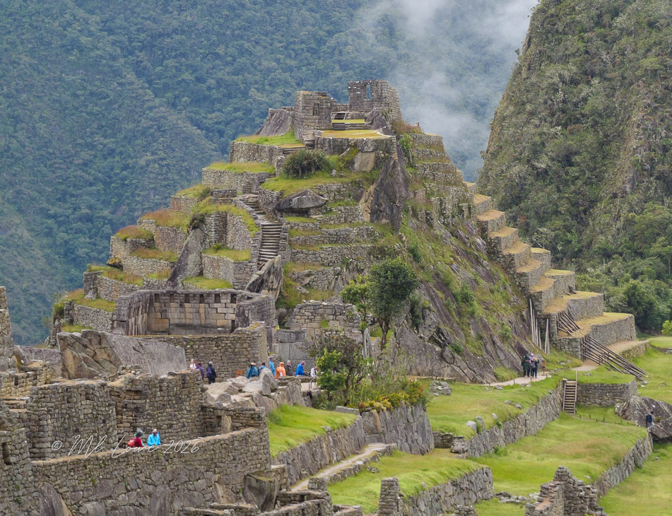 A panoramic view of Machu Picchu, featuring ancient stone structures, terraces, and lush green mountains under a cloudy sky.