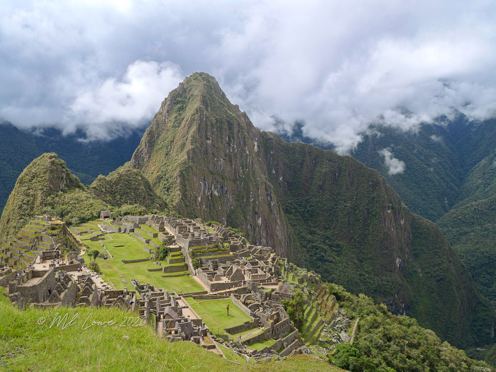 A panoramic view of Machu Picchu, an ancient Incan city, set against a backdrop of steep mountains and cloudy skies.