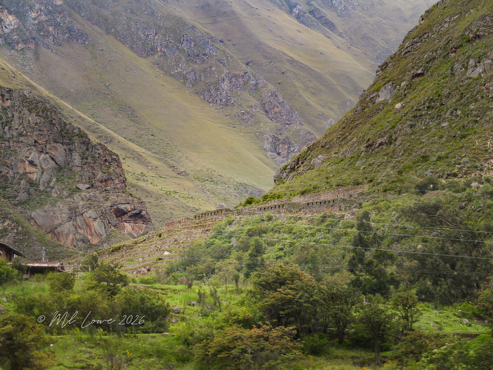 A scenic view of mountains and hills, showcasing a stone wall along the hillside, with lush green vegetation in the foreground and rocky terrain in the background.