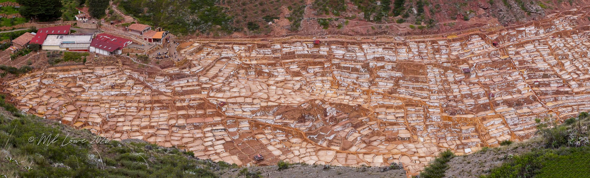 A panoramic view of the Maras salt mines in Peru, showcasing a series of terraced salt evaporating ponds set against a mountainous backdrop.