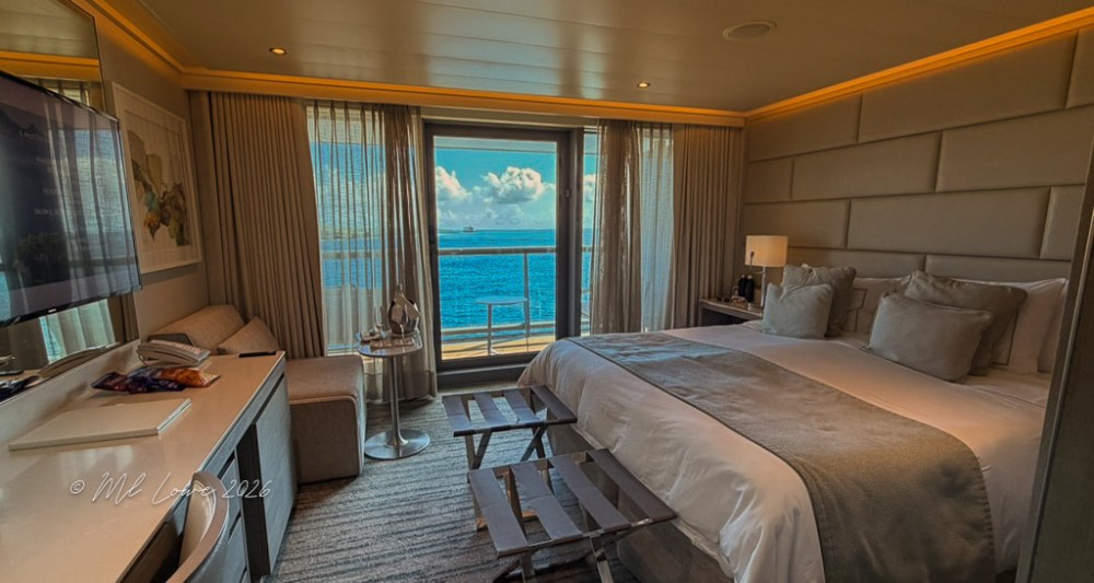 Modern hotel room with a large bed, TV, and panoramic ocean view through a balcony window.