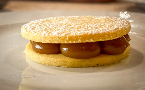 A delicate dessert consisting of two buttery cookies stacked with a creamy filling and dusted with powdered sugar.